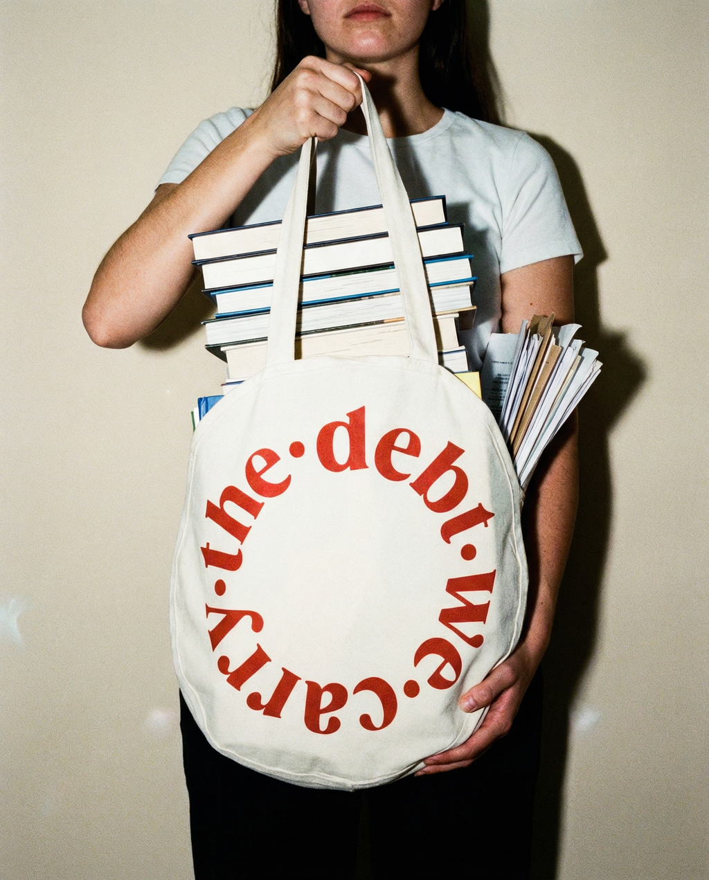 Person holding a tote bag with 'the debt we carry' text and books.