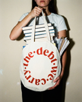 Person holding a tote bag with 'the debt we carry' text and books.