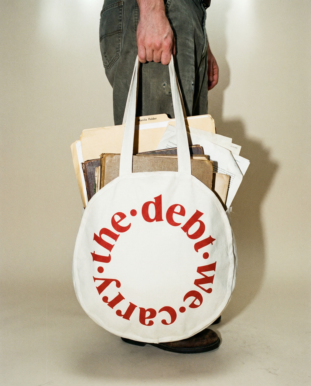 Person holding a tote bag with 'the debt we carry' text, filled with books.